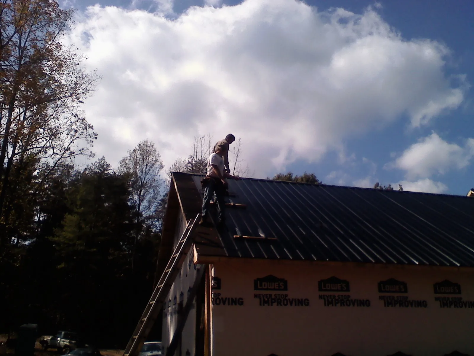 Roofer fastening dark metal panels high against a cloudy sky, from a Roof Inspection job in Jones